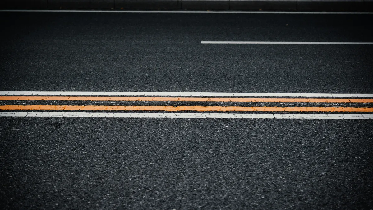 Two orange lines and white edge lines painted on dark asphalt