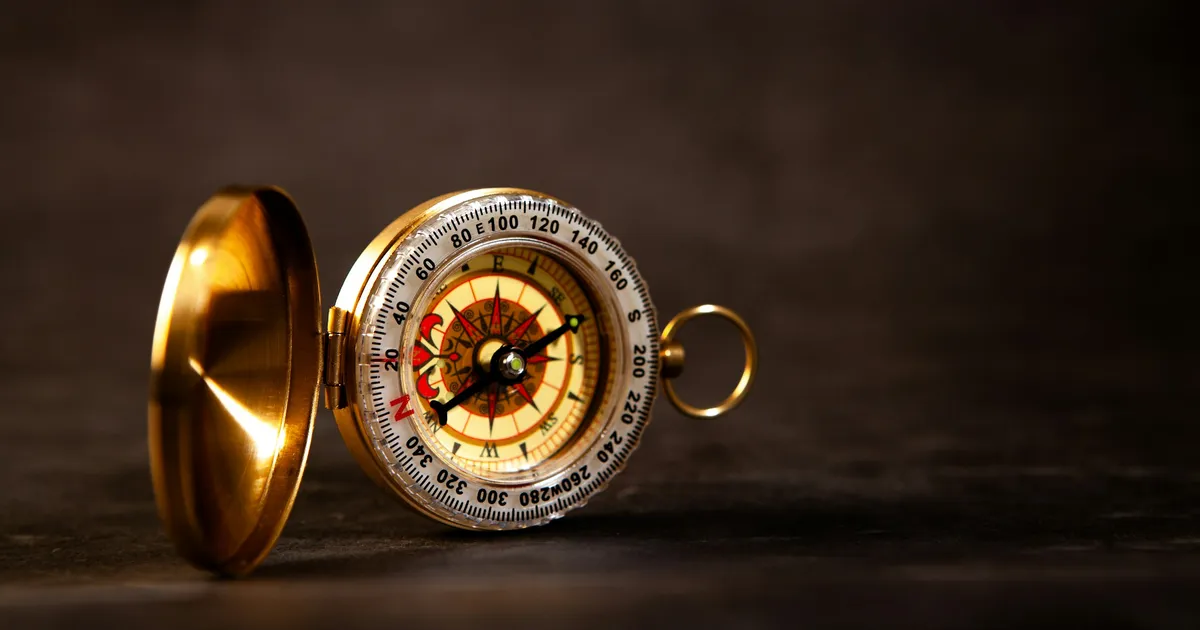 A vintage brass compass with its lid open on a dark surface, needle pointing north