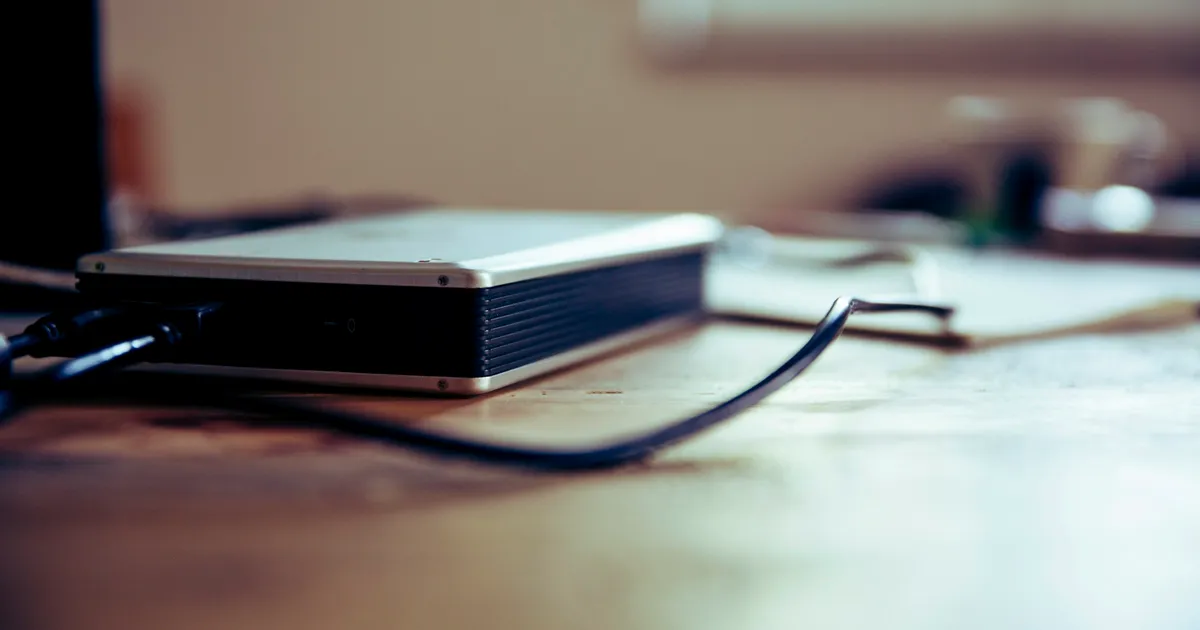 A portable external hard drive lying on a wooden desk with a cable trailing away