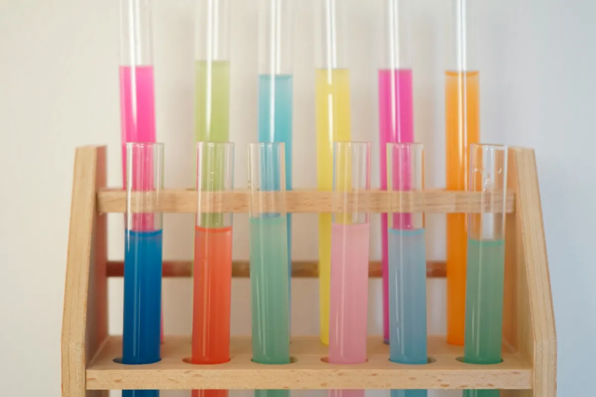 A wooden rack of glass test tubes filled with brightly colored liquids