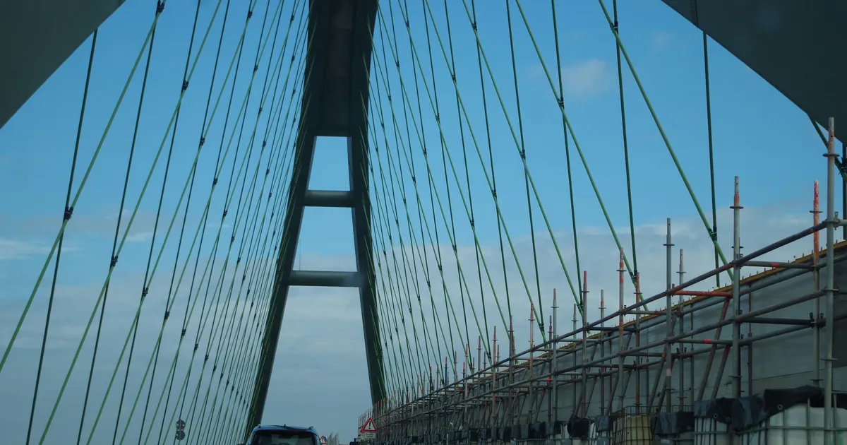 A cable-stayed bridge tower with green cables and scaffolding against a blue sky