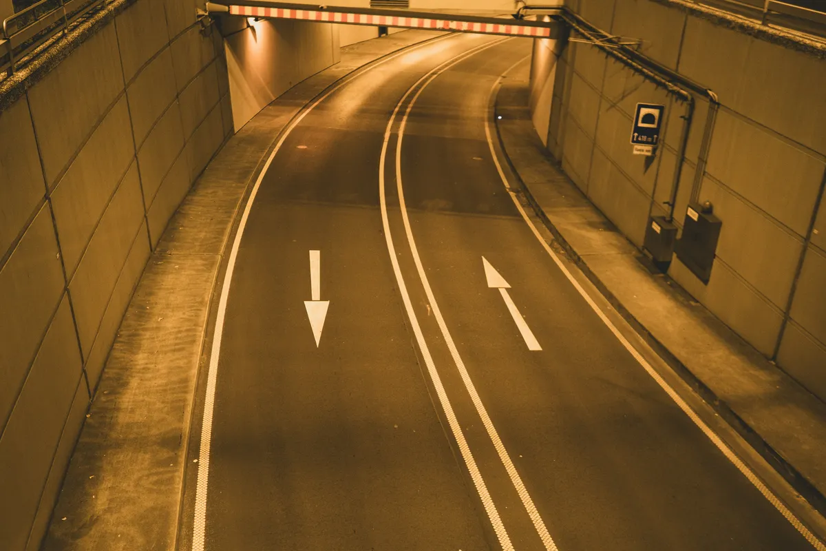 Curved tunnel road with white direction arrows and double lane lines under warm light