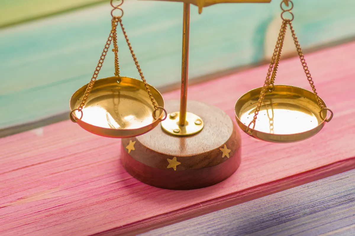 A small gold balance scale resting on colorful painted wood, weighing two options