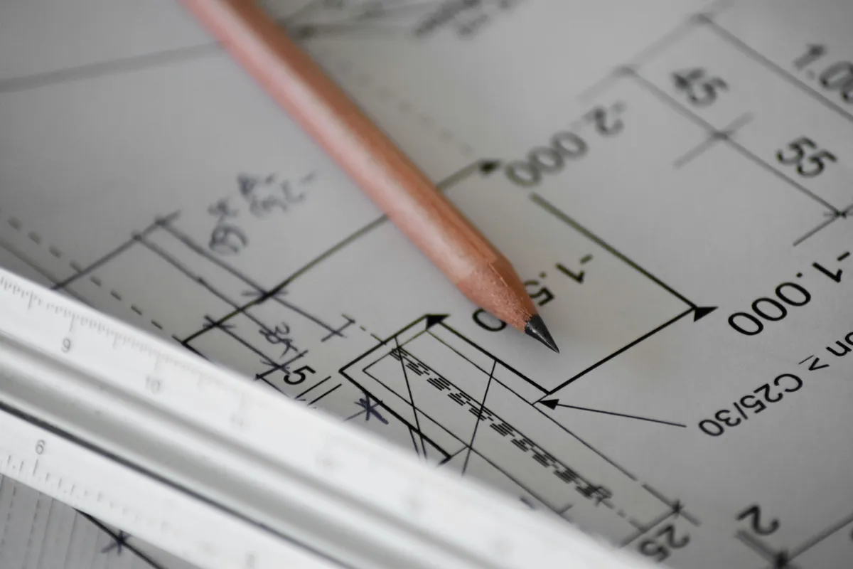 Pencil resting on a dimensioned technical drawing next to an architect scale ruler