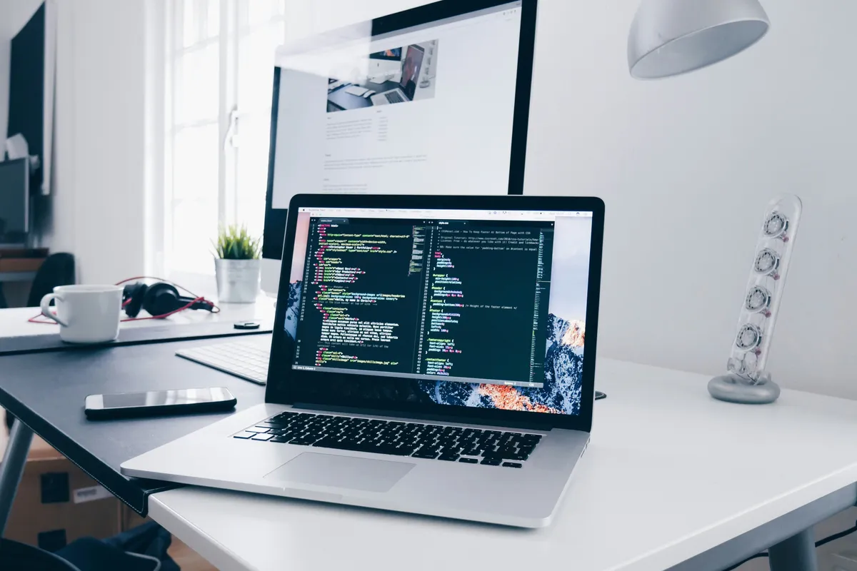 A MacBook showing lines of code on a busy developer desk beside a coffee cup