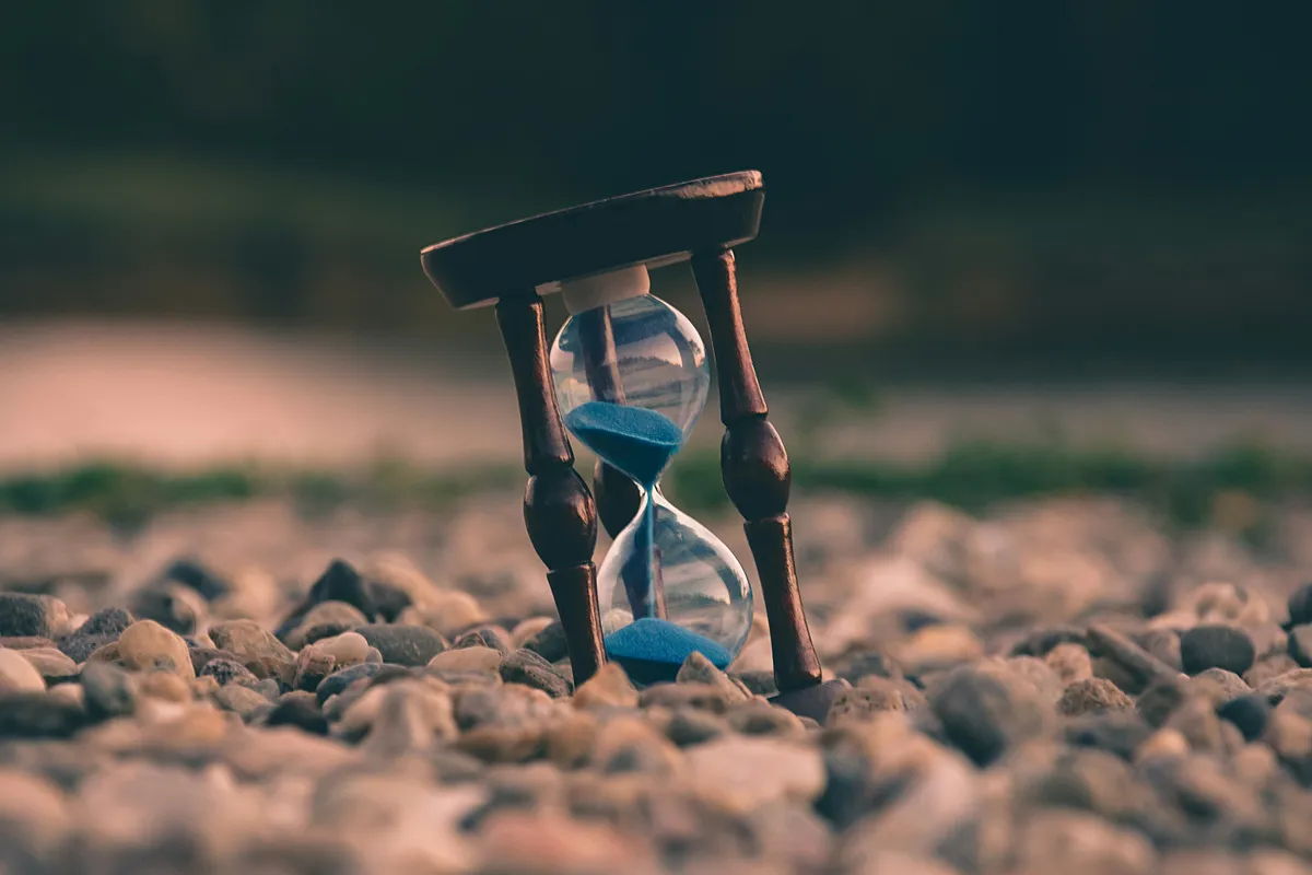 A small wooden hourglass with blue sand resting on a bed of stones