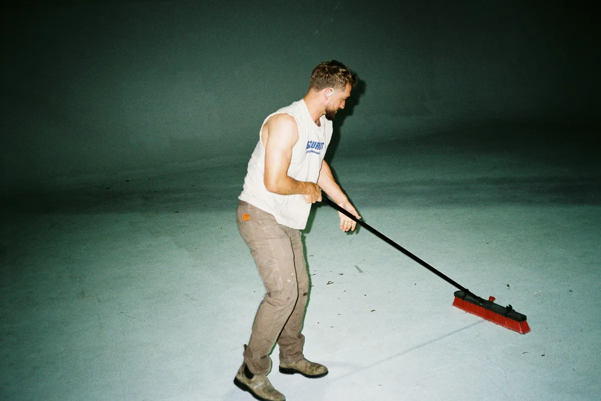 A man sweeping the floor of a large empty room with a long broom