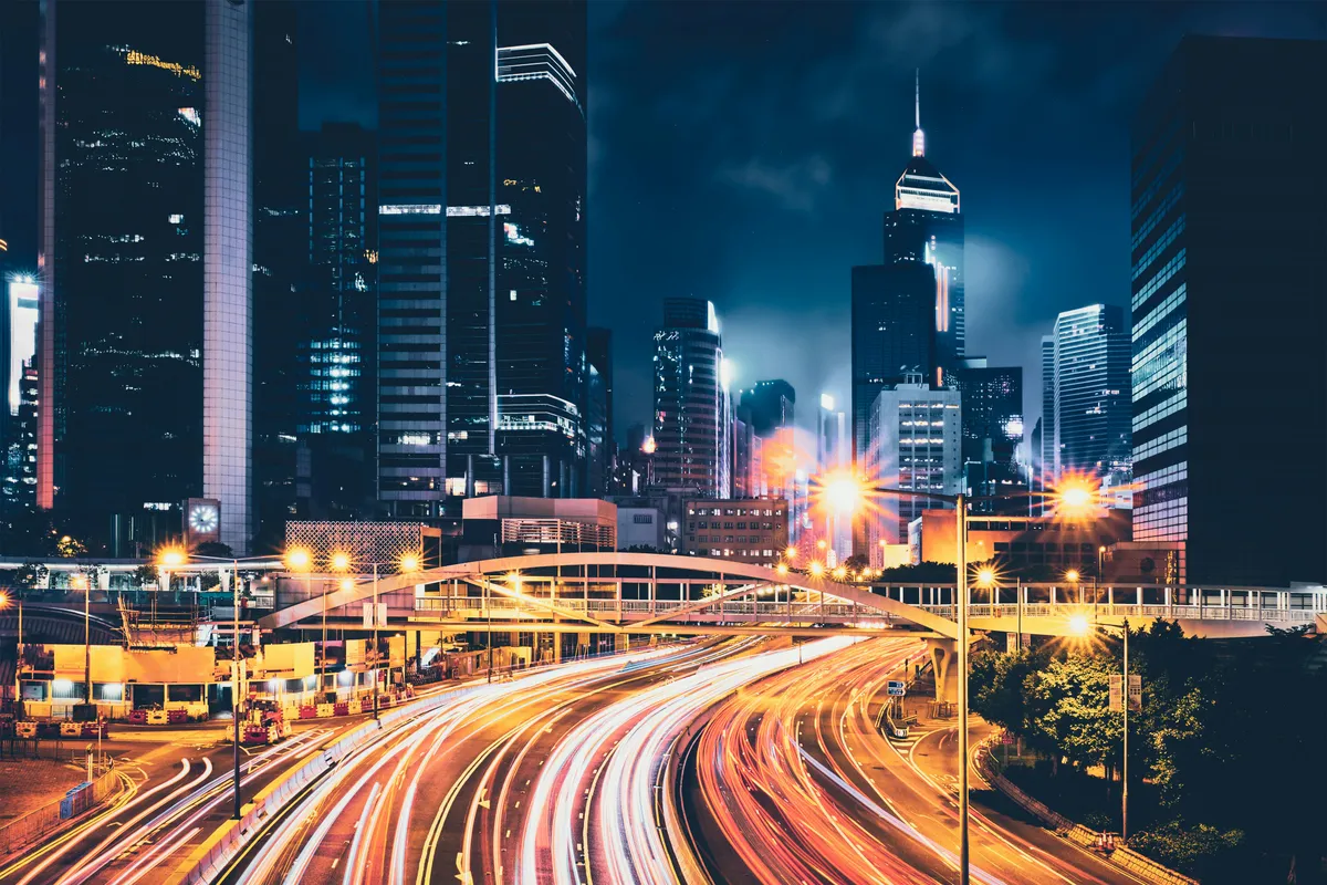 Long-exposure light trails from city traffic streaming beneath illuminated skyscrapers at night