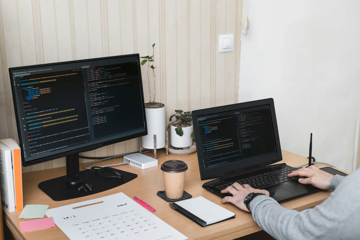 A tidy developer desk with a monitor and laptop both showing TypeScript code