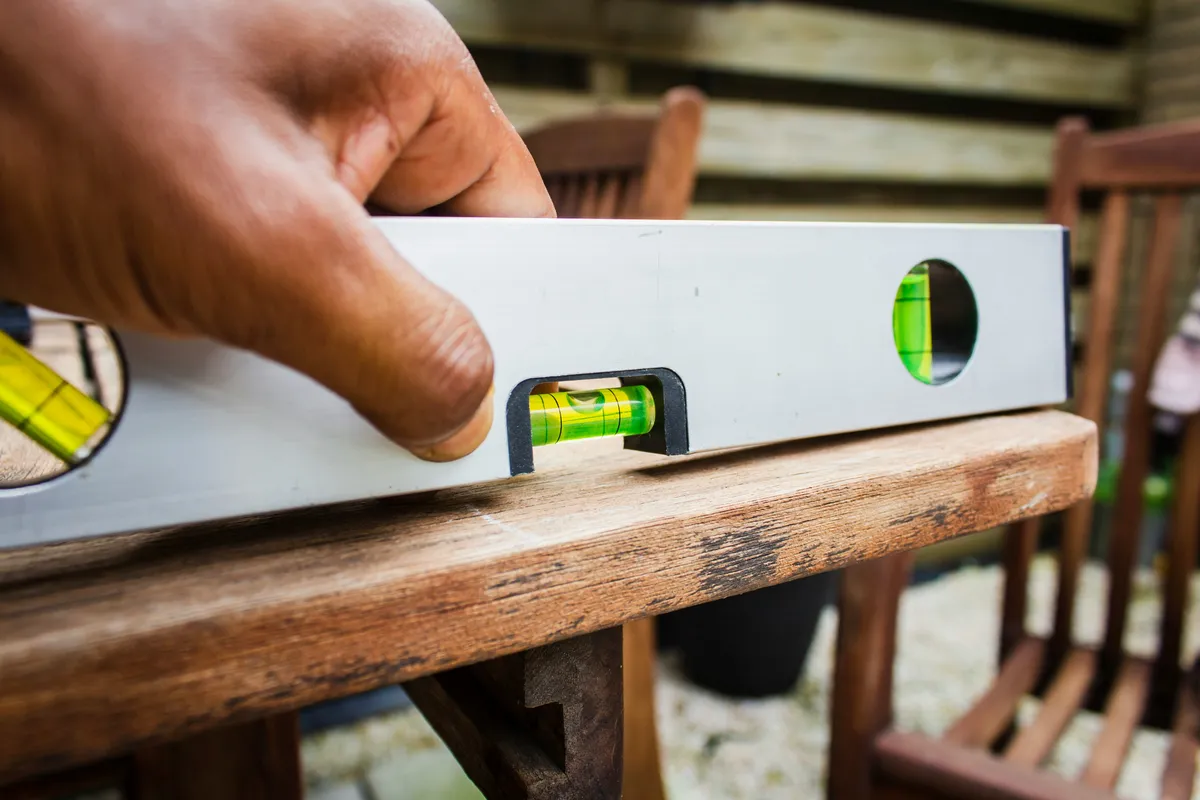 A hand holding a metal spirit level against the edge of a weathered wooden table