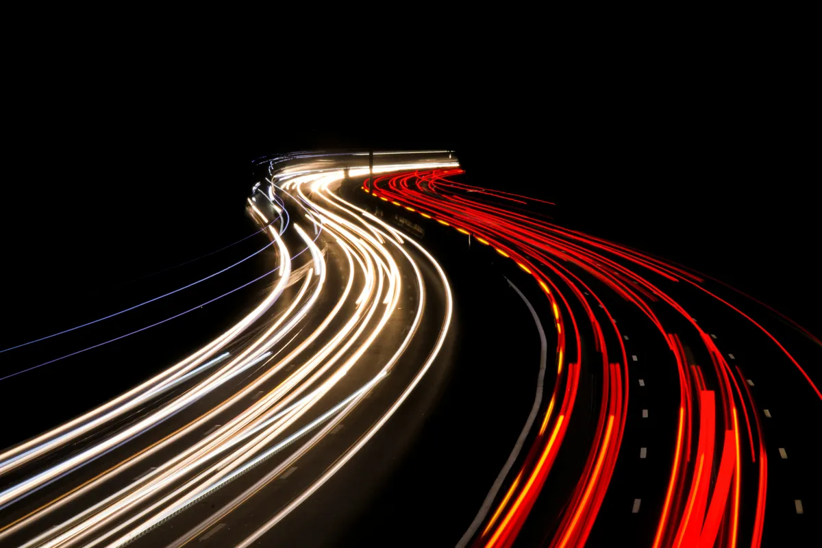 Long-exposure light trails streaming along a curving highway at night